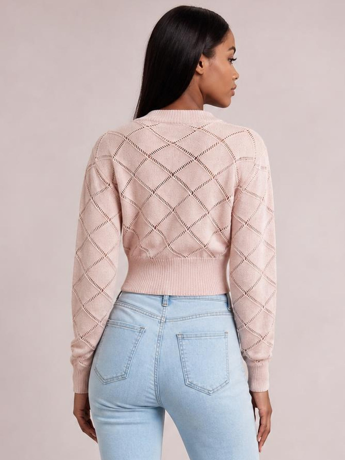 Model shown from the back wears a blush pink openwork plaid cropped sweater with a round neck, long sleeves, and ribbed cuffs and hem.