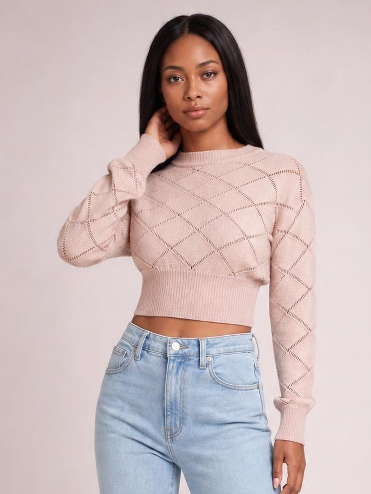 Model poses in a blush pink openwork plaid cropped sweater with a round neck, long sleeves, and ribbed cuffs and waistband.