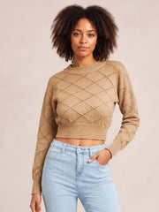 Model wearing a tan openwork plaid cropped sweater with a ribbed round neck, long sleeves, and fitted ribbed hem, posing with one hand in her jeans pocket.