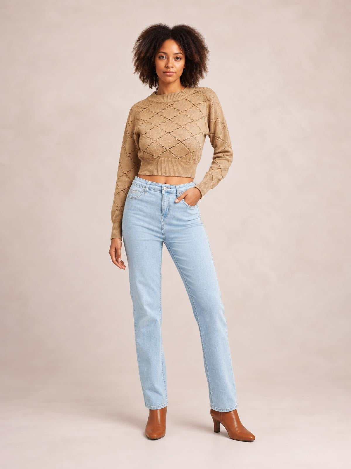 Model wears a tan openwork plaid cropped sweater with a round neck, long sleeves, ribbed cuffs and hem, standing with one hand in her jeans pocket.