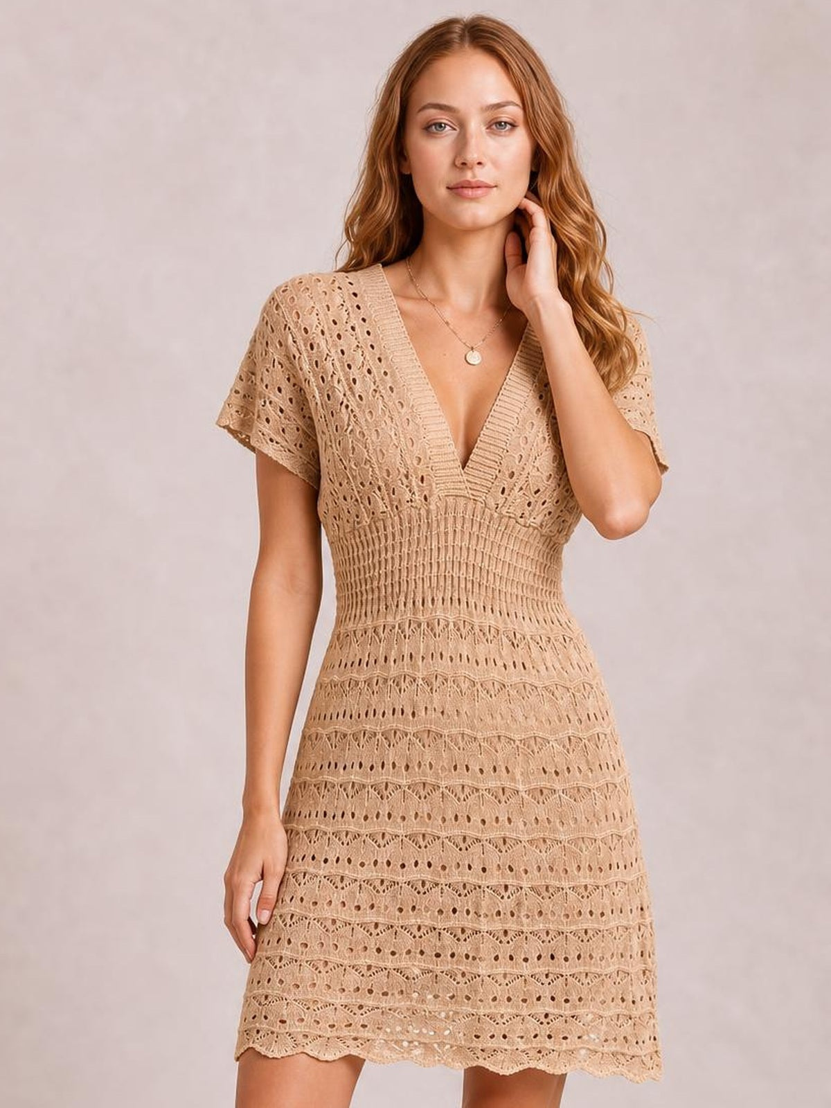 A model poses in a beige semi-sheer openwork cover-up dress with short sleeves, a plunging V-neckline, fitted waist, and flared skirt.