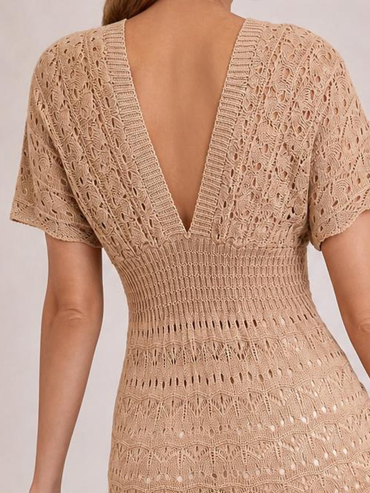 A model wears a beige semi-sheer openwork cover-up dress with short sleeves, a deep V-back, ribbed trim, and a fitted waist.