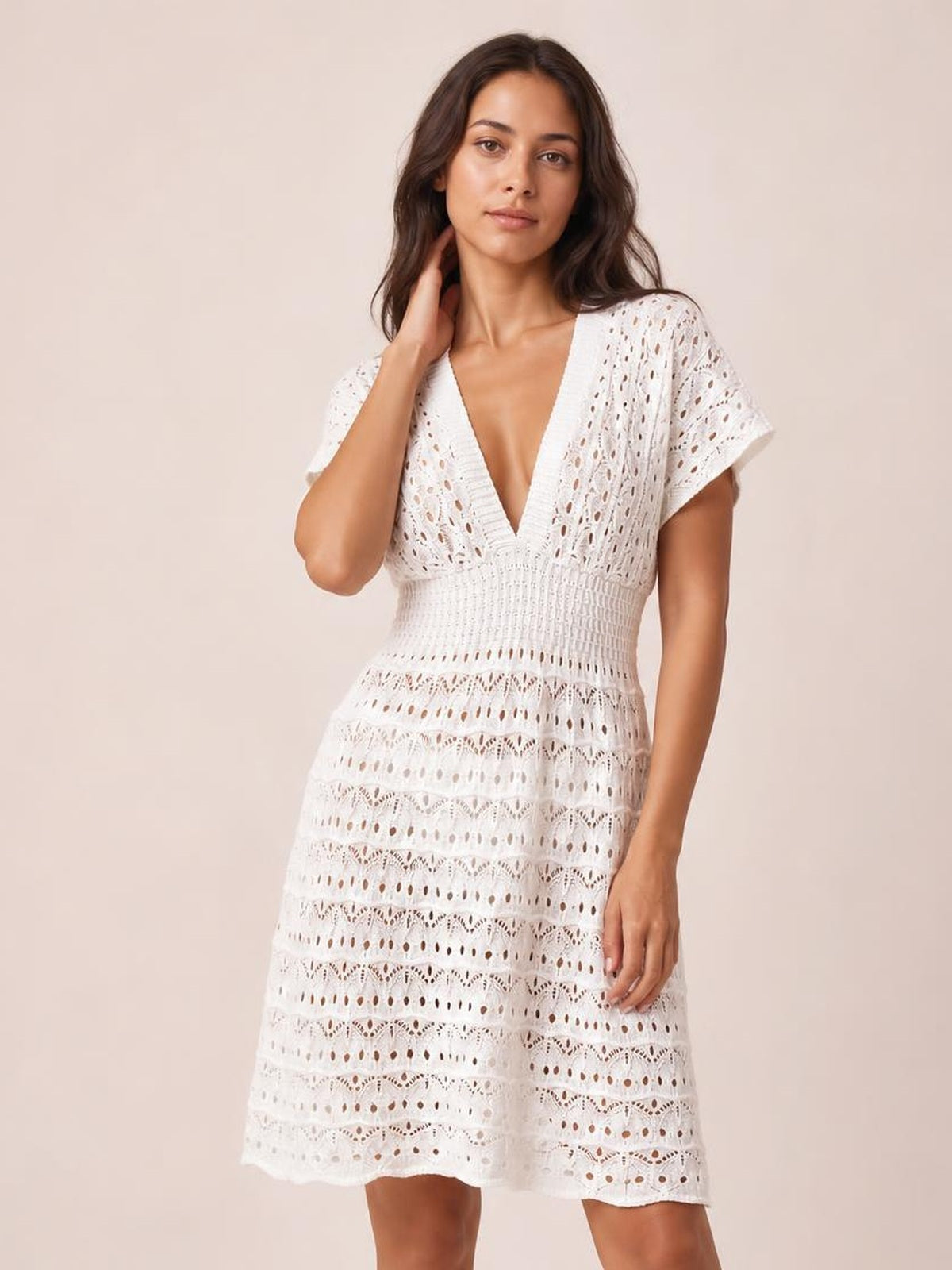 A model poses in a white semi-sheer openwork cover-up dress with short sleeves, a plunging neckline, fitted waist, and flared knee-length silhouette.