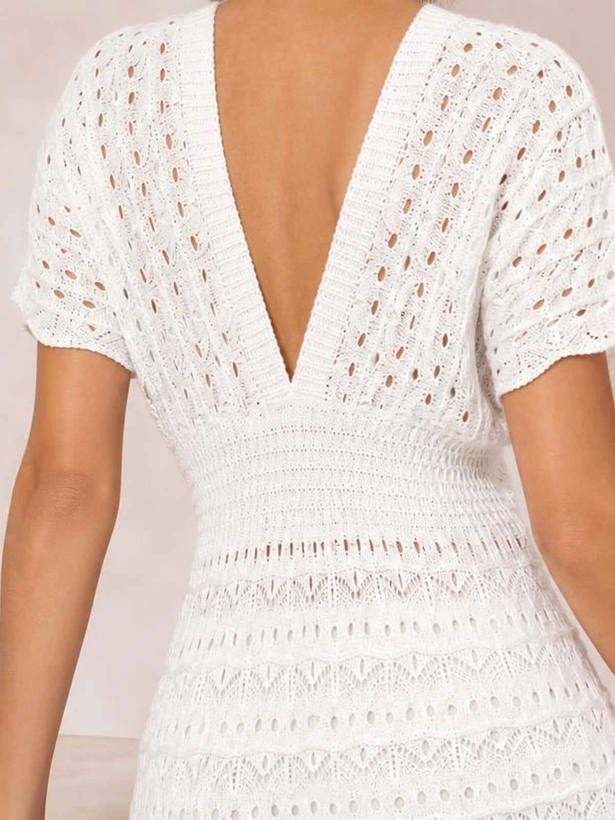 A model wears a white semi-sheer openwork cover-up dress with short sleeves, a plunging V-neckline, fitted waist, and tiered flared silhouette.