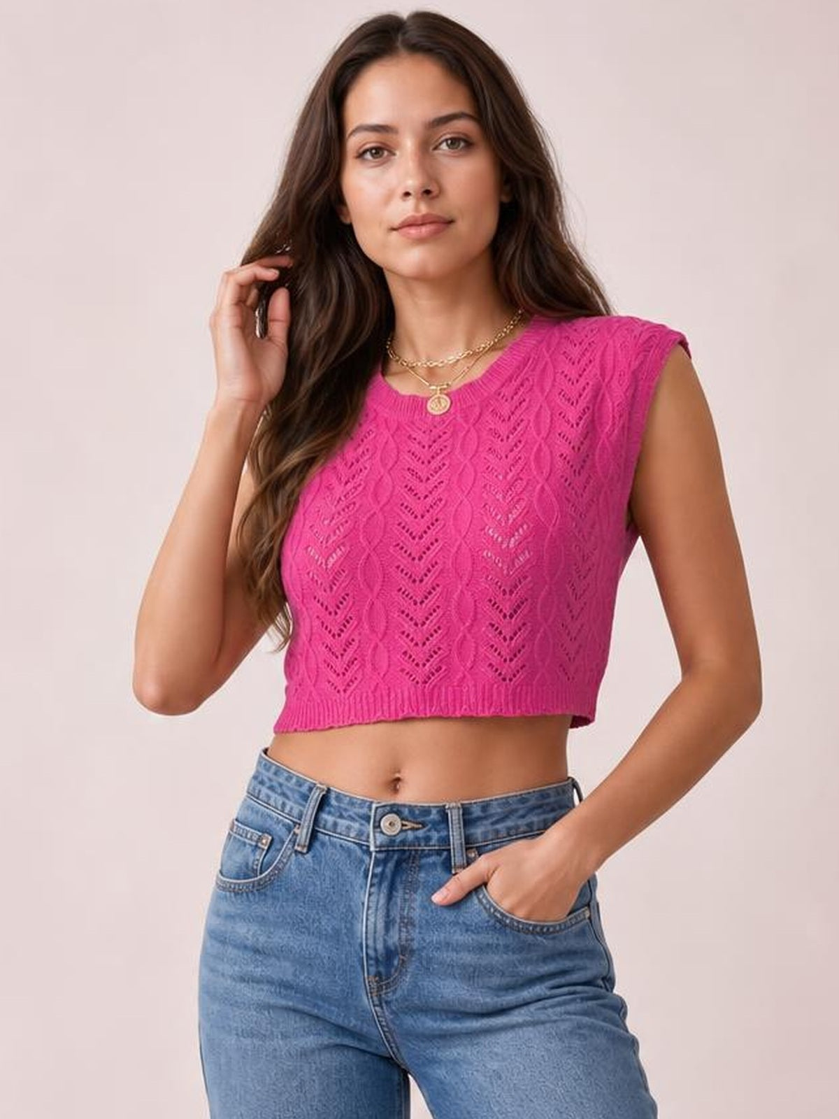 A model poses in a bright pink openwork knit top with a round neck, cap sleeves, cropped fitted silhouette, and ribbed hem.