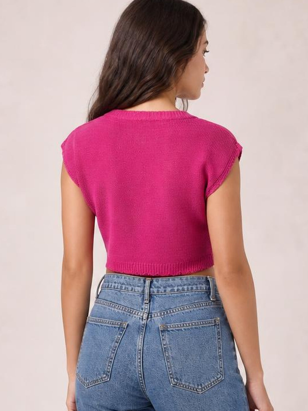 Model shown from the back in a bright pink knit top with a round neck, cap sleeves, ribbed edges, and a cropped silhouette.