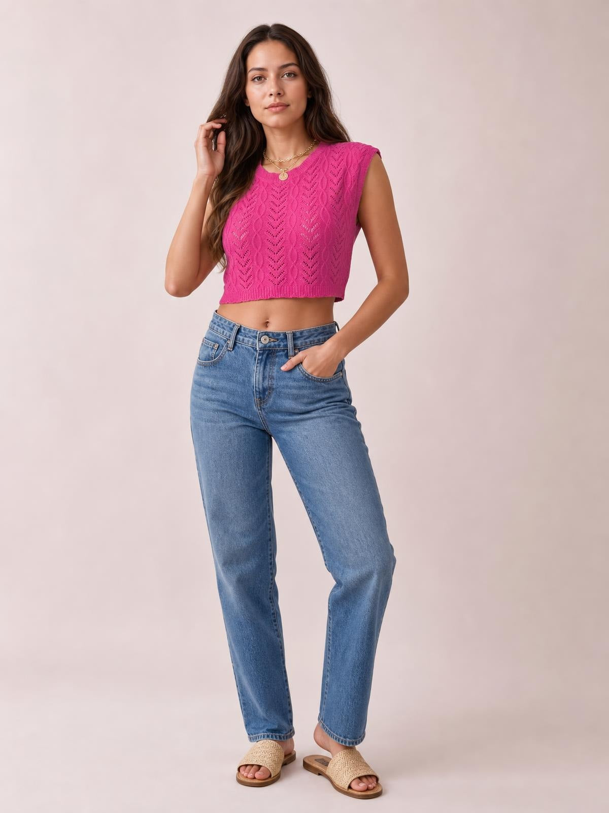A model poses in a bright pink openwork knit top with a round neck, cap sleeves, cropped silhouette, and textured vertical pattern.