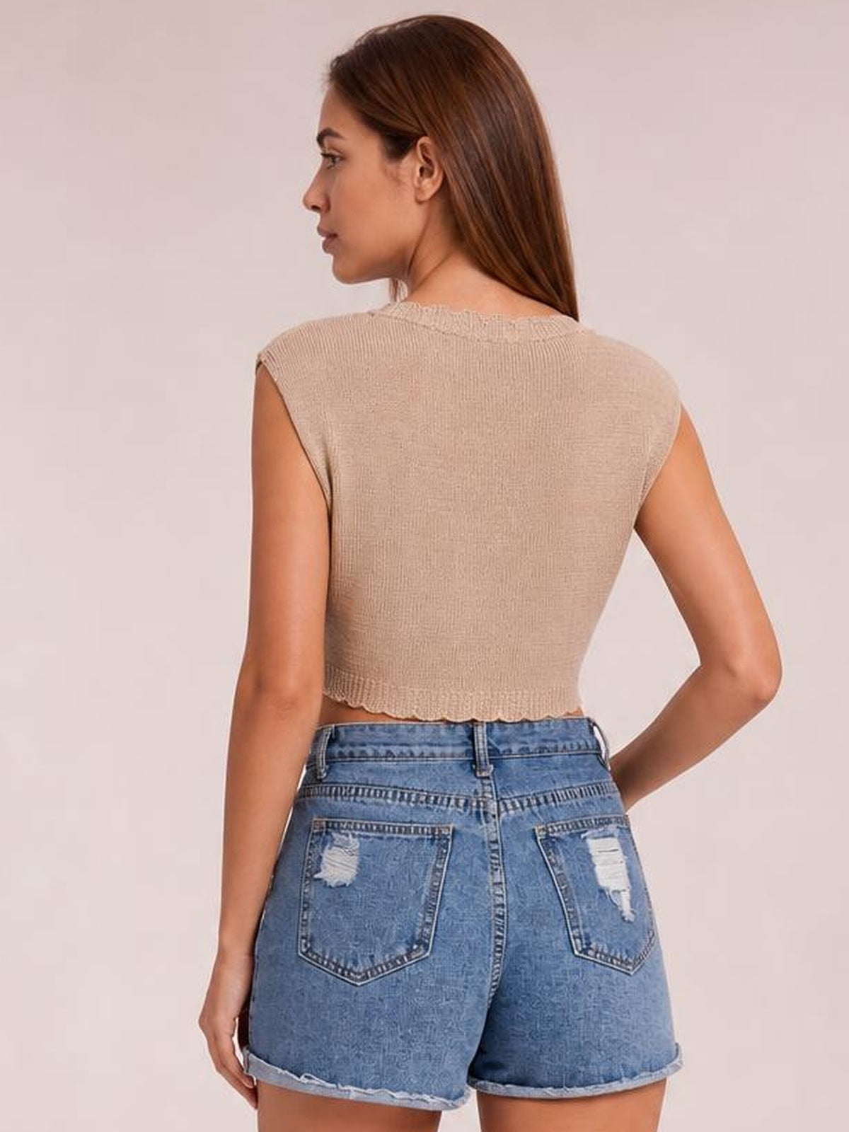 A model poses in a beige openwork round-neck cap-sleeve knit top with a fitted cropped silhouette and scalloped hem, viewed from the back.
