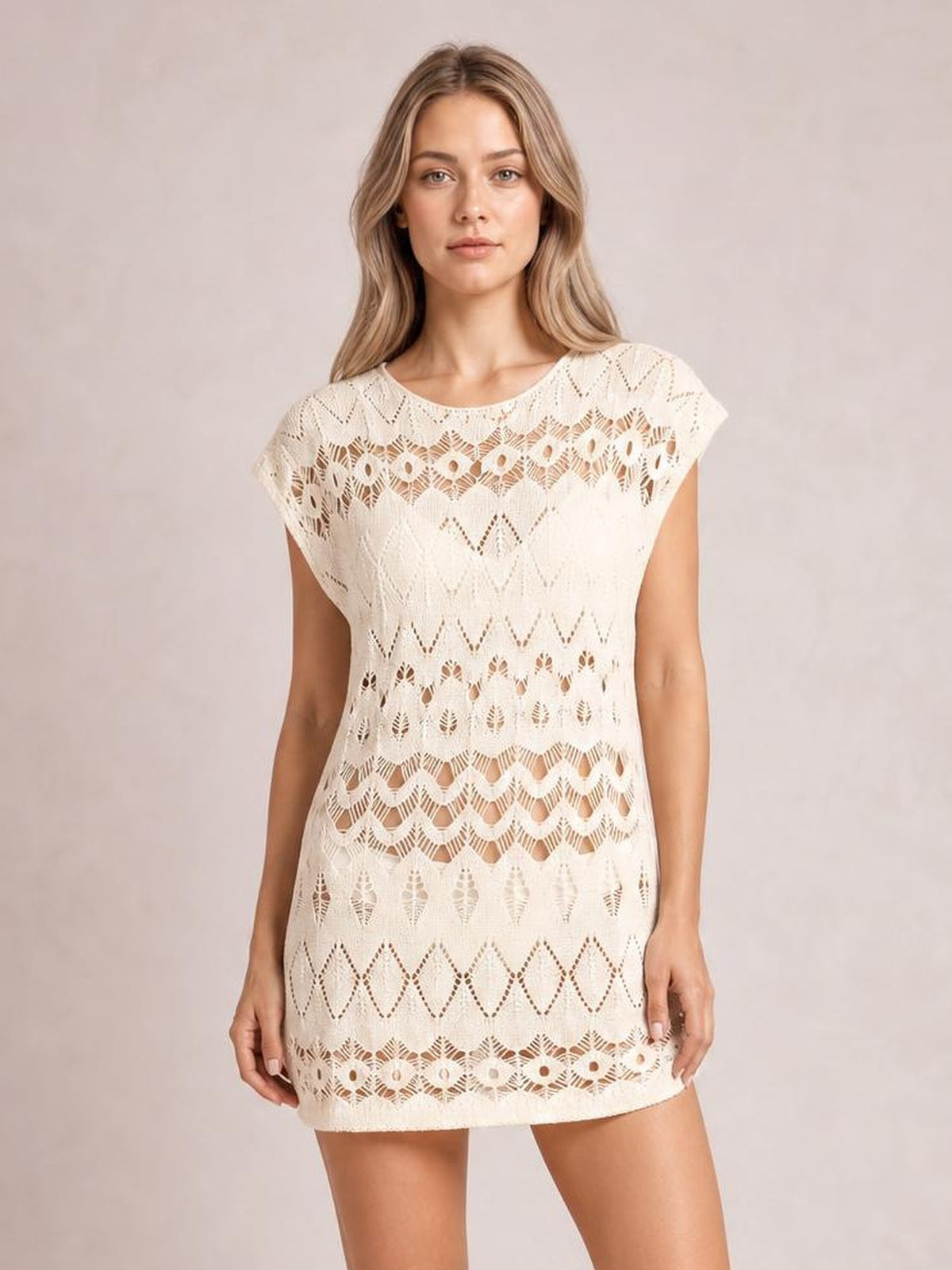 Model stands facing forward in an ivory openwork round neck cover-up with a short-sleeve silhouette, geometric patterned construction, and straight mini-length hem.