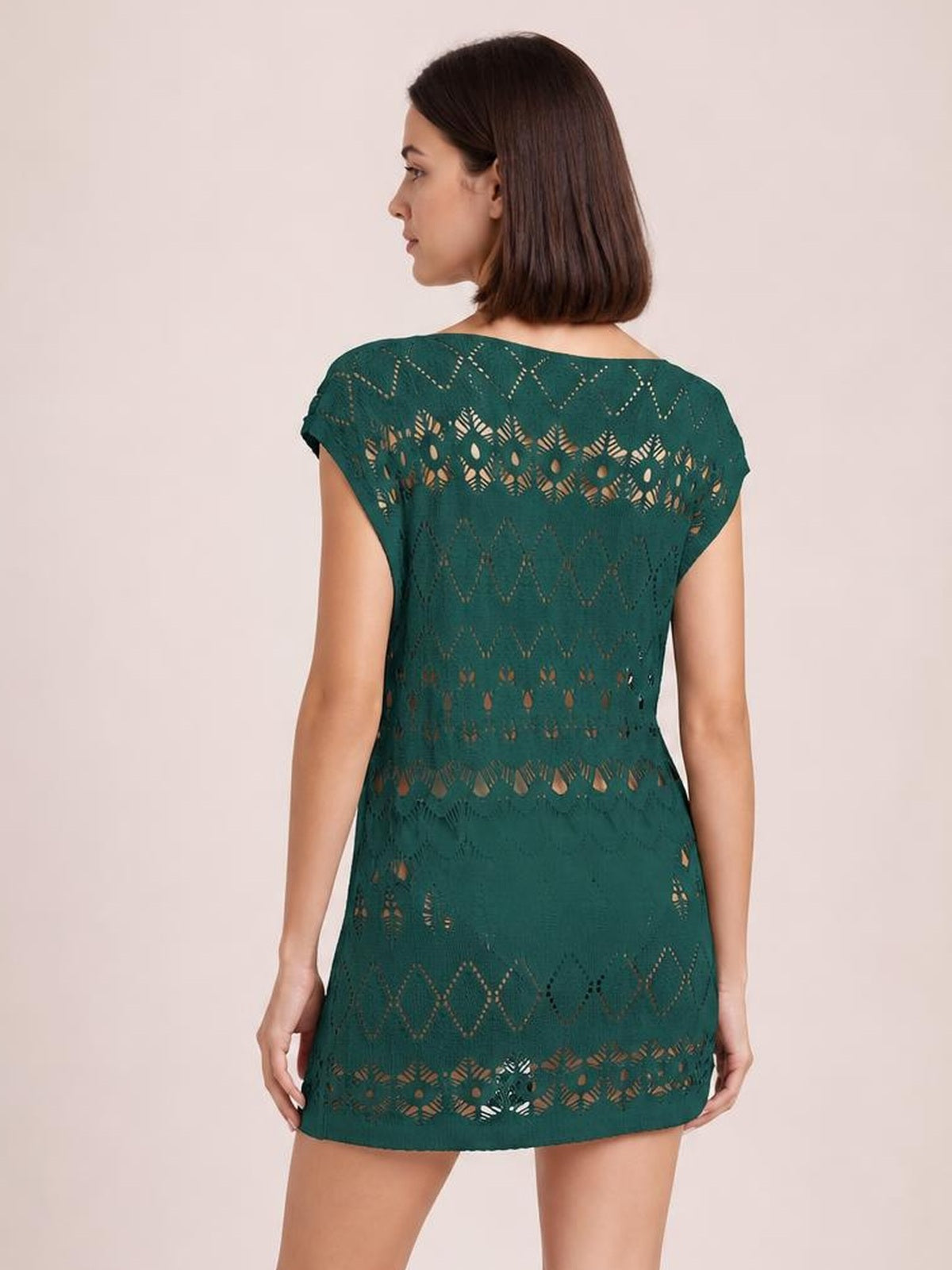 A model poses from the back in a dark teal openwork round-neck cover-up with short sleeves, a relaxed tunic silhouette, and patterned cutout bands.