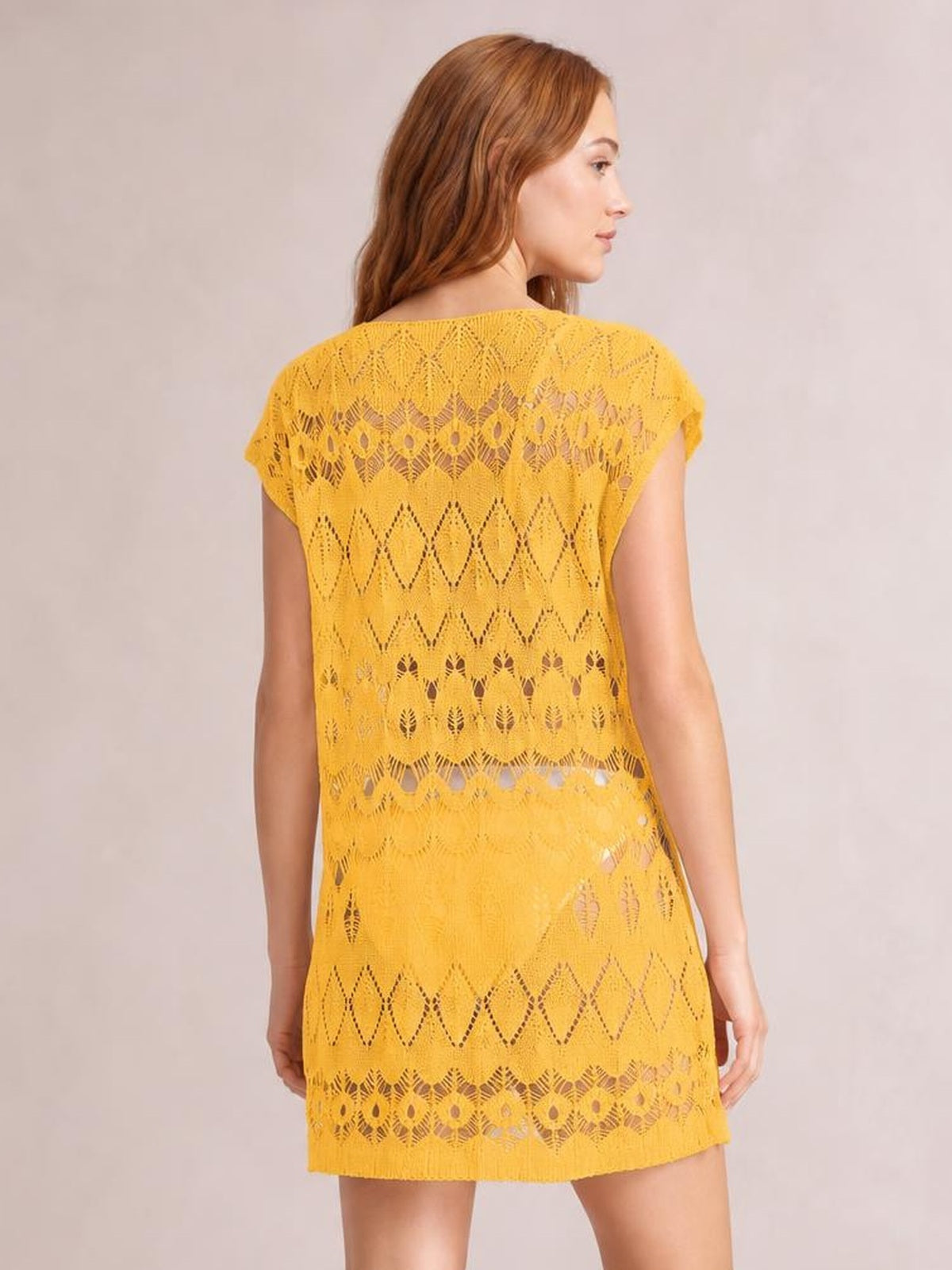A model looks over her shoulder wearing a yellow openwork round neck cover-up with short sleeves, geometric patterns, and a relaxed tunic-length silhouette.