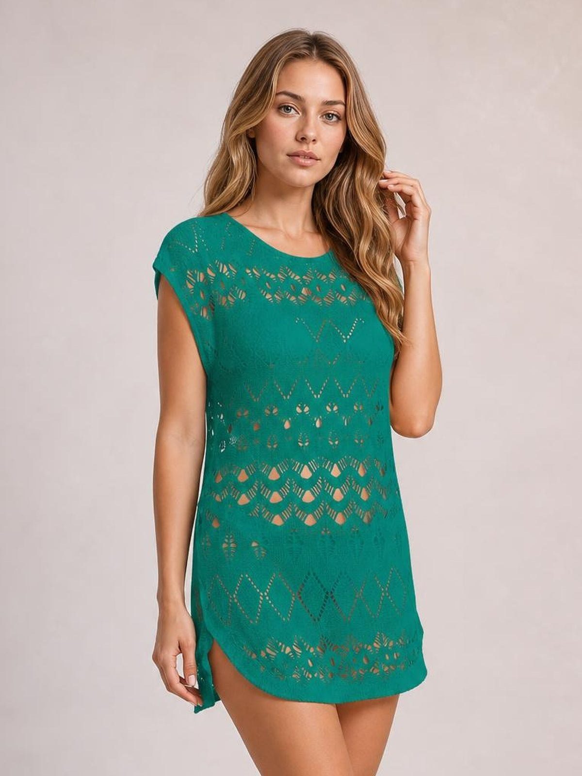 A model poses in a teal openwork round neck cover-up with cap sleeves, a relaxed straight silhouette, patterned cutouts, and a curved mini-length hem.