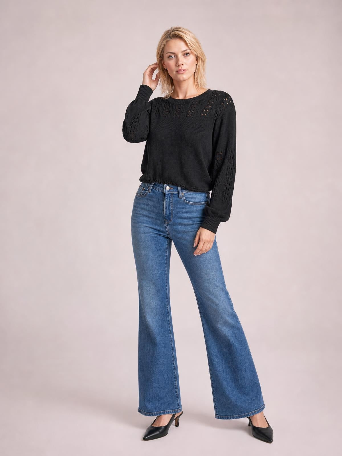 Model poses in a black openwork round neck long sleeve sweater with ribbed cuffs and hem, styled with wide-leg blue jeans.