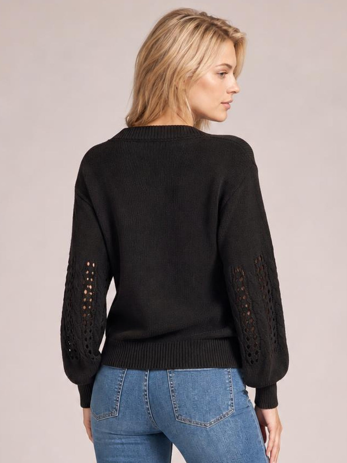 Back view of a model wearing a black openwork round neck sweater with long sleeves, ribbed cuffs and hem, and a relaxed silhouette.