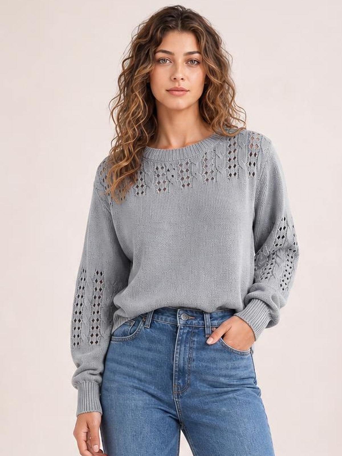 A model poses in a relaxed gray openwork round neck sweater with long sleeves, ribbed cuffs and hem, and a loose silhouette, one hand in her jeans pocket.
