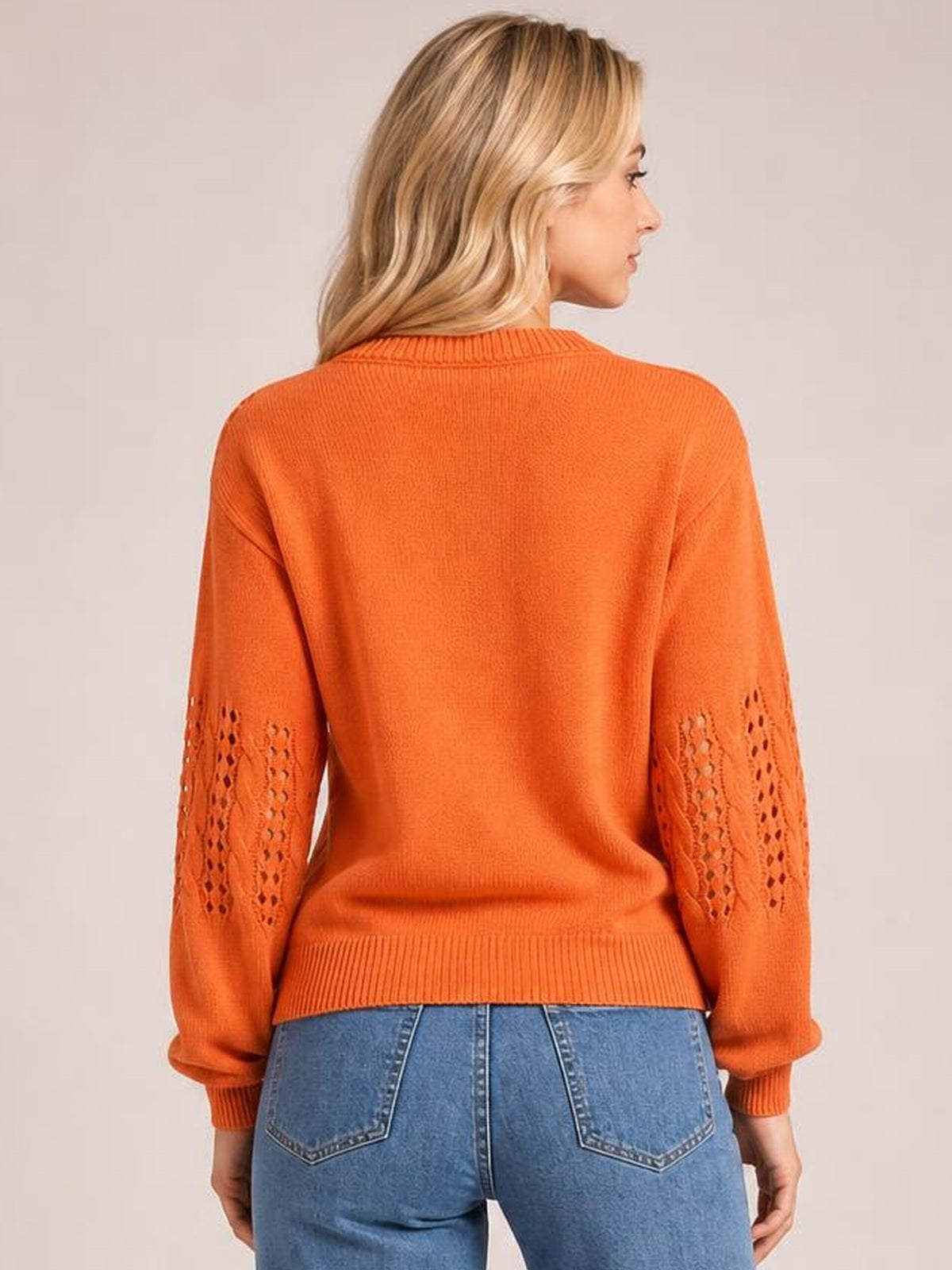 Model shown from the back wears an orange openwork long-sleeve sweater with a round neckline, ribbed cuffs and hem, and a relaxed silhouette.