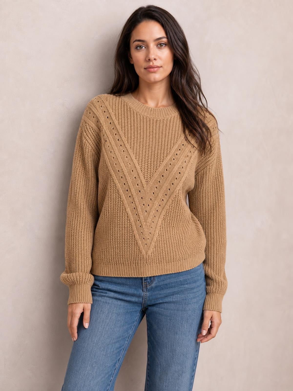 Model wears a camel openwork round neck sweater with long sleeves, ribbed cuffs and hem, and a relaxed silhouette over blue jeans.