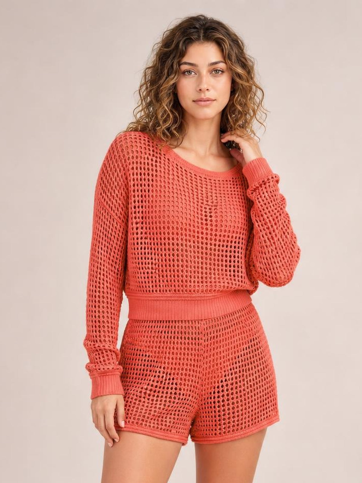 A model wears a coral two-piece cover-up set with a round-neck openwork long-sleeve top, ribbed trim, and matching relaxed shorts.