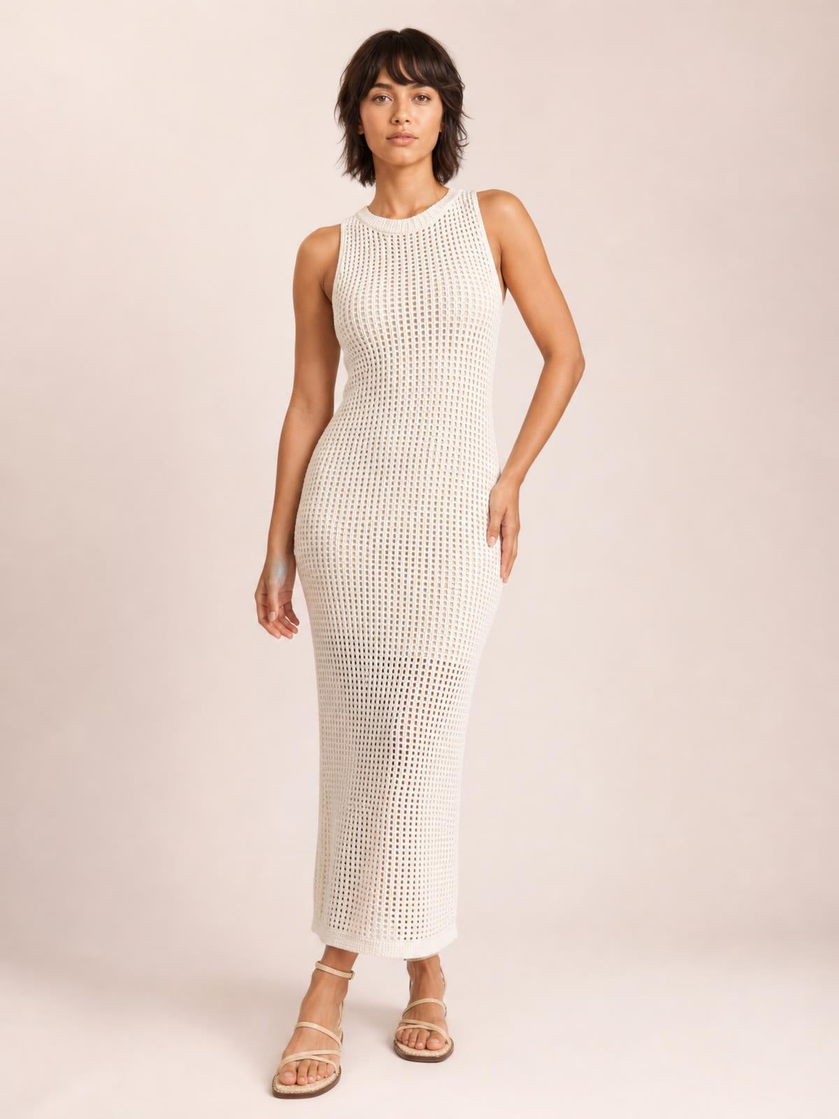 A model poses in a white, semi-sheer openwork cover-up with a round neck, sleeveless cut, side slit, and fitted ankle-length silhouette.