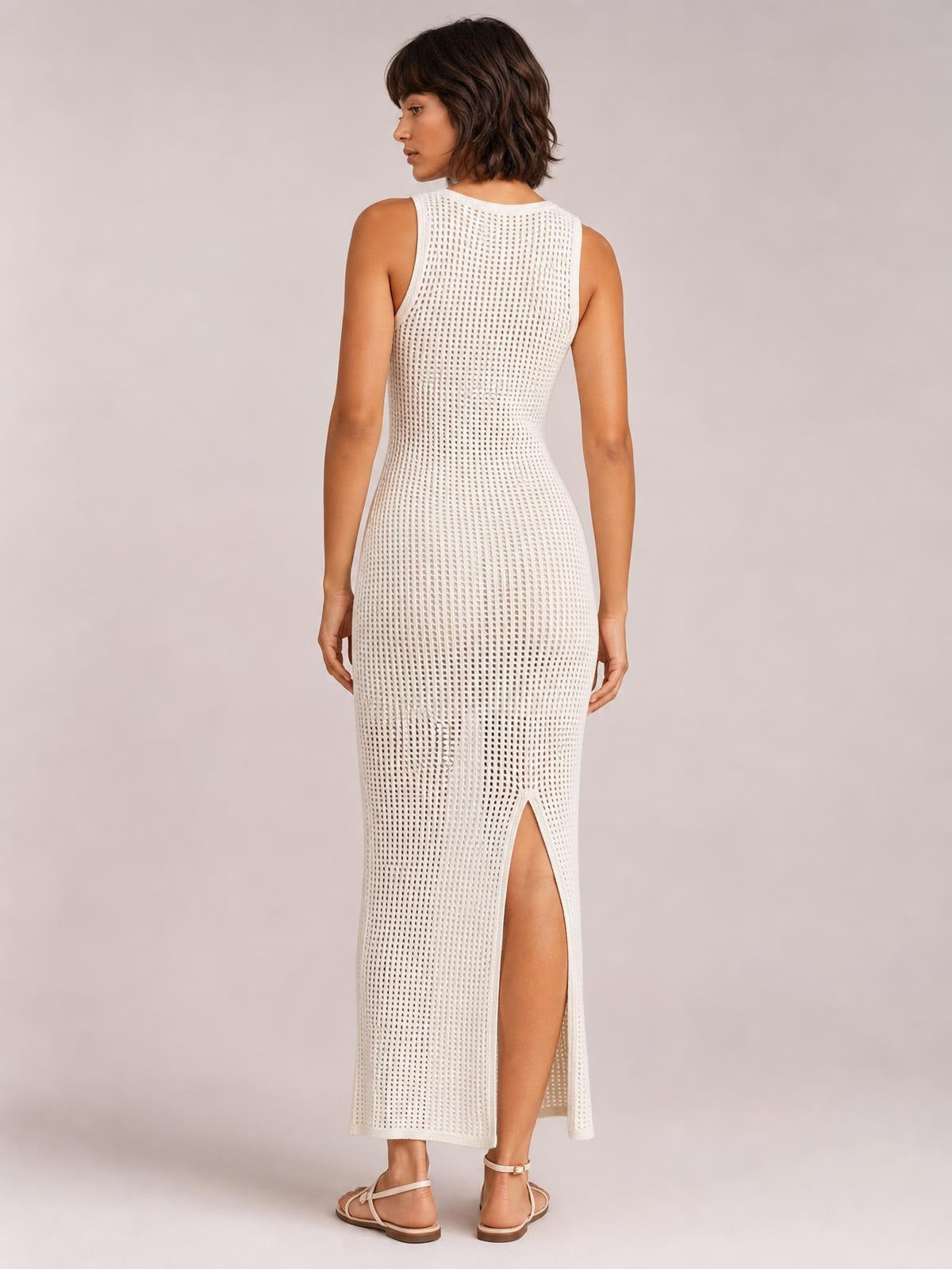 A model poses from the back wearing a white semi-sheer openwork cover-up with a fitted silhouette, round neck, sleeveless construction, and side slit.
