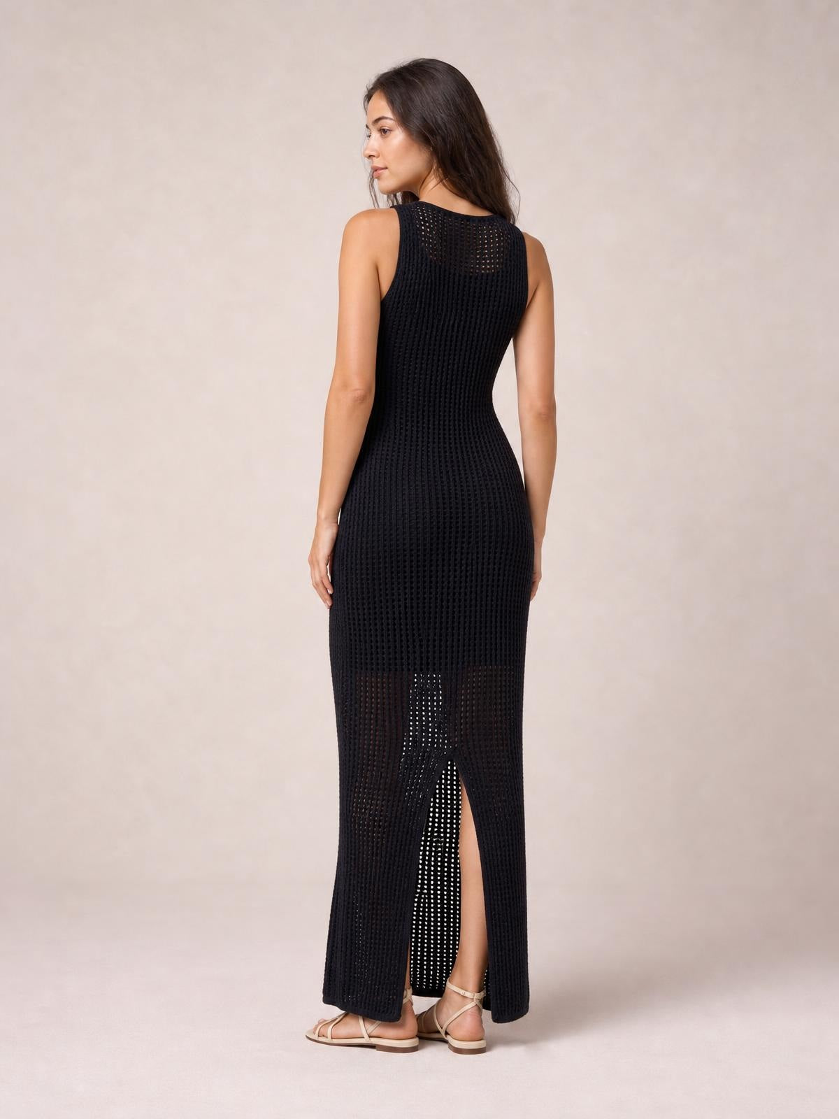 Back view of a model in a black, semi-sheer openwork cover-up with a round neck, sleeveless cut, fitted maxi silhouette, and high back slit.