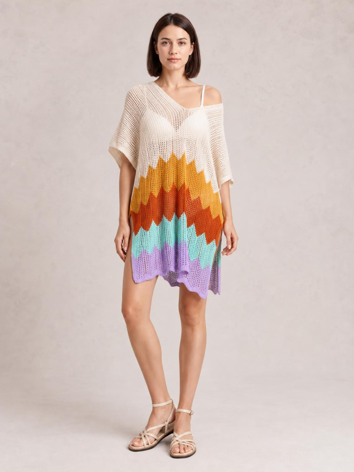 Model stands with one leg crossed, wearing a loose openwork V-neck half-sleeve cover-up in cream with colorful zigzag stripes and a scalloped hem.