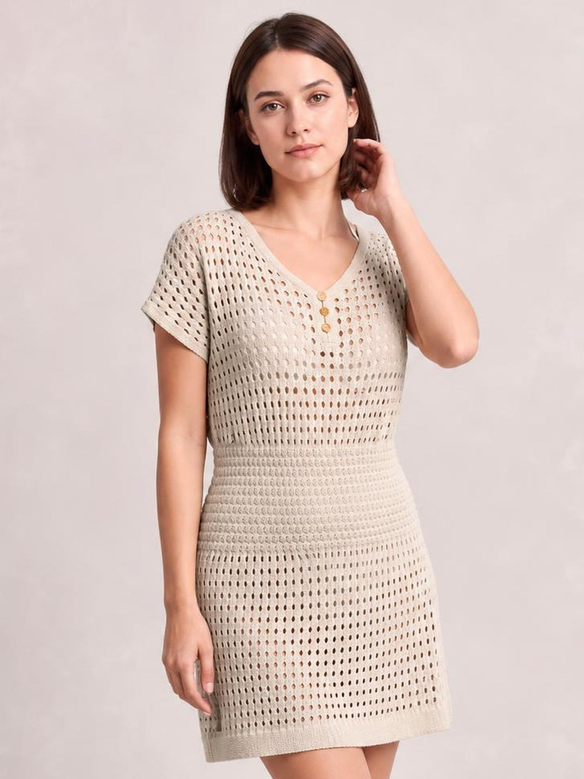 Model poses in a beige semi-sheer openwork cover up with a V-neck, short sleeves, button-front detail, fitted waist, and straight mini-length silhouette.