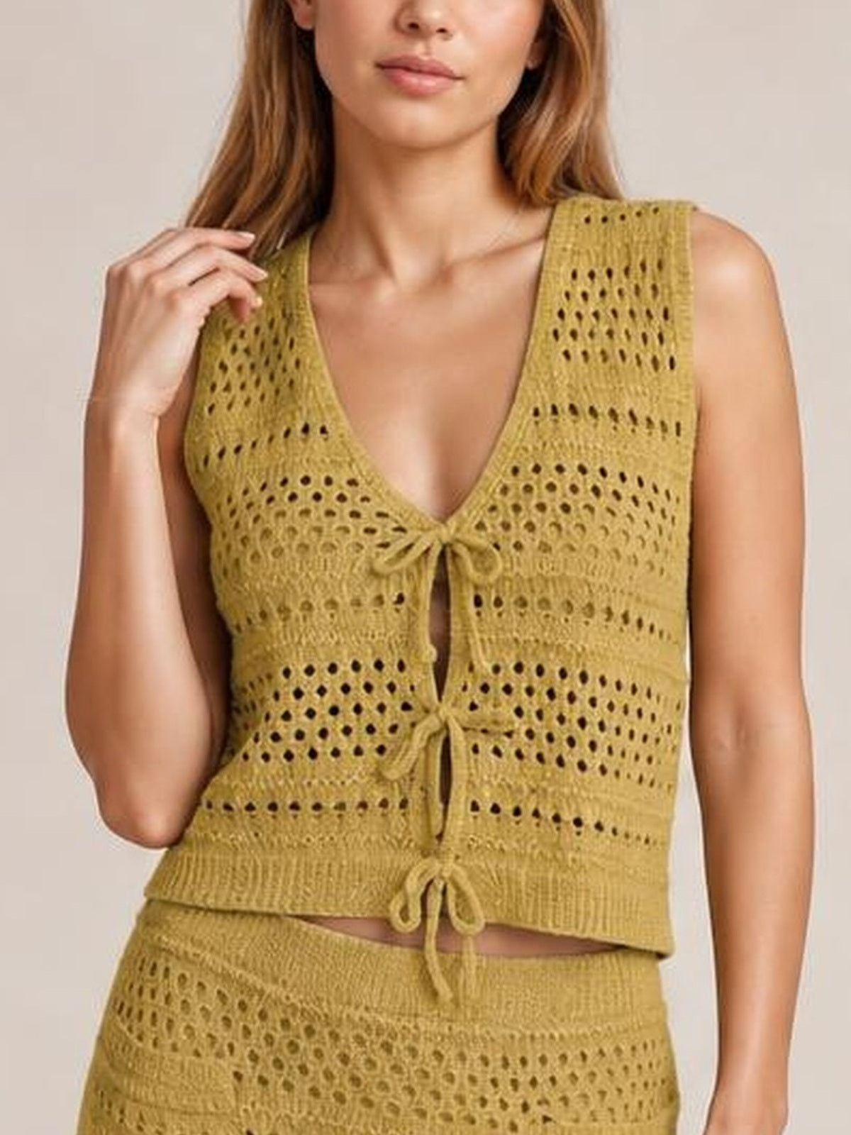 Model poses with one hand in her hair, wearing a mustard openwork knit cover-up set with a V-neck tied top and coordinating skirt.