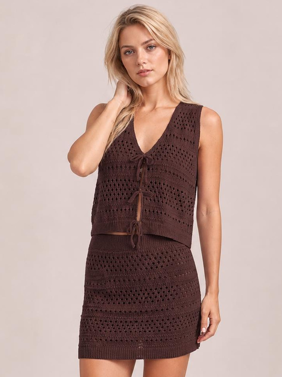 Model wearing a dark brown openwork knit cover-up set with a tied V-neck top and coordinating fitted mini skirt.