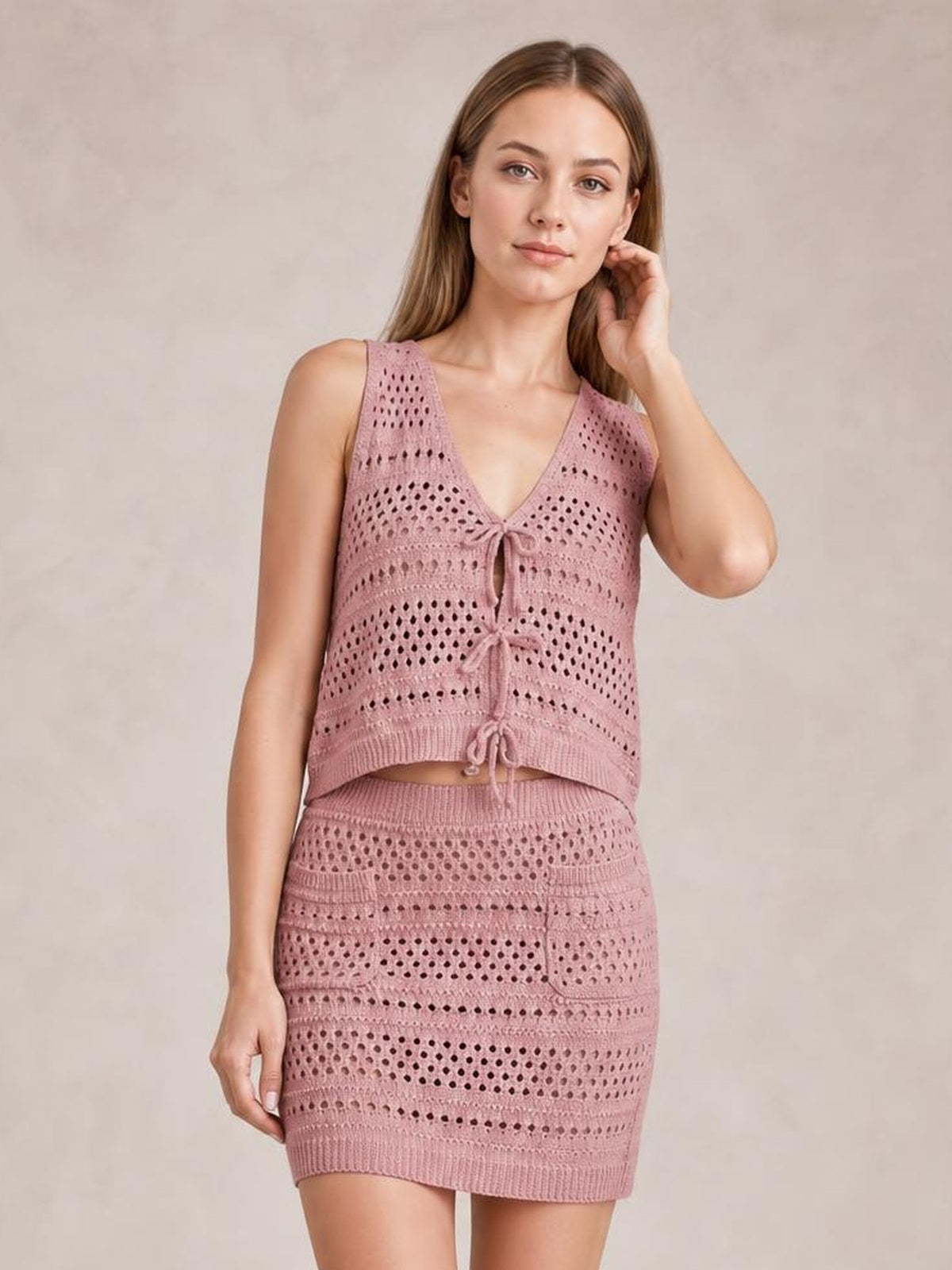 Model wearing a dusty rose openwork V-neck knit cover-up set with a tied sleeveless top, fitted skirt, and front pockets.