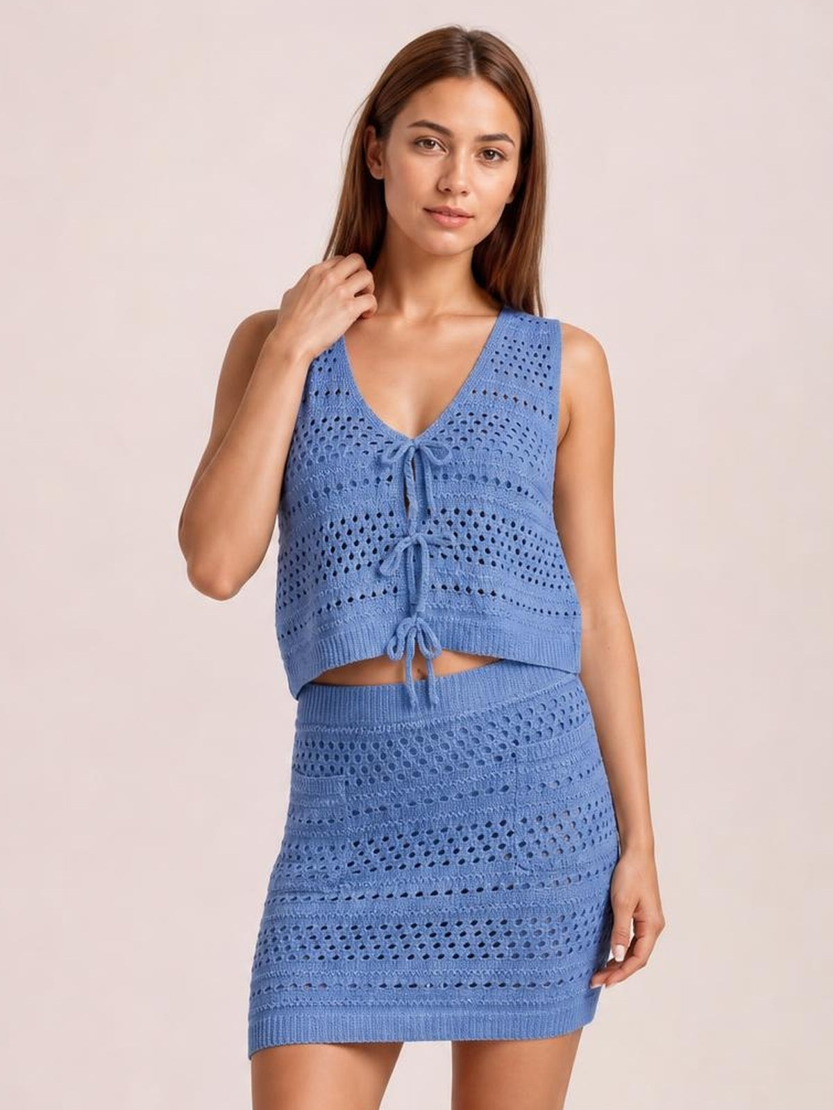 Model poses in a blue openwork knit cover-up set with a tied V-neck top, cropped silhouette, and fitted mini skirt.