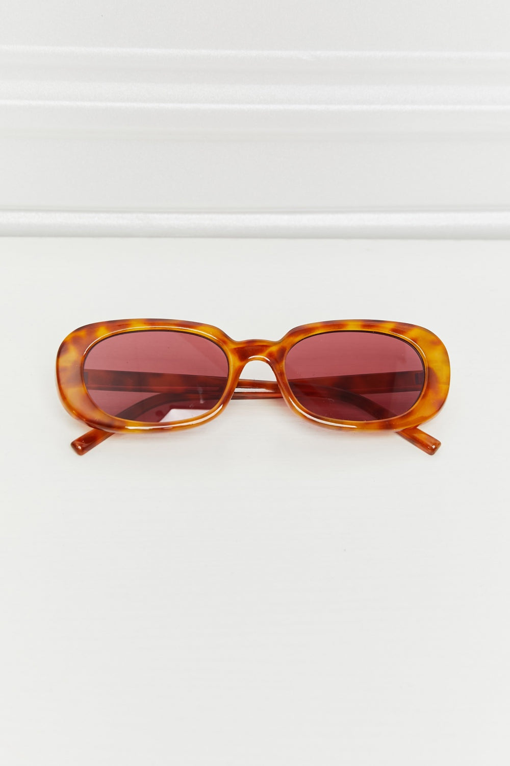 Oval full-rim sunglasses in translucent amber tortoiseshell feature softly curved reddish lenses, a defined bridge, and matching polycarbonate temples.