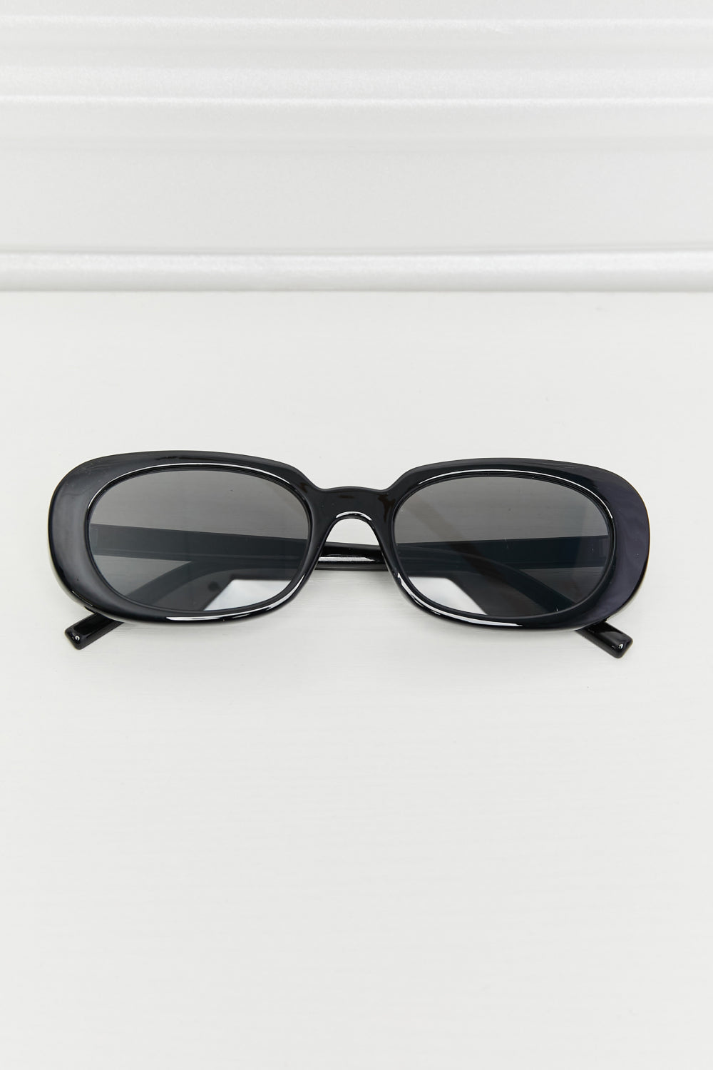 Black oval full-rim sunglasses with softly curved dark lenses, a polished thick frame, defined bridge, and temples extending outward.