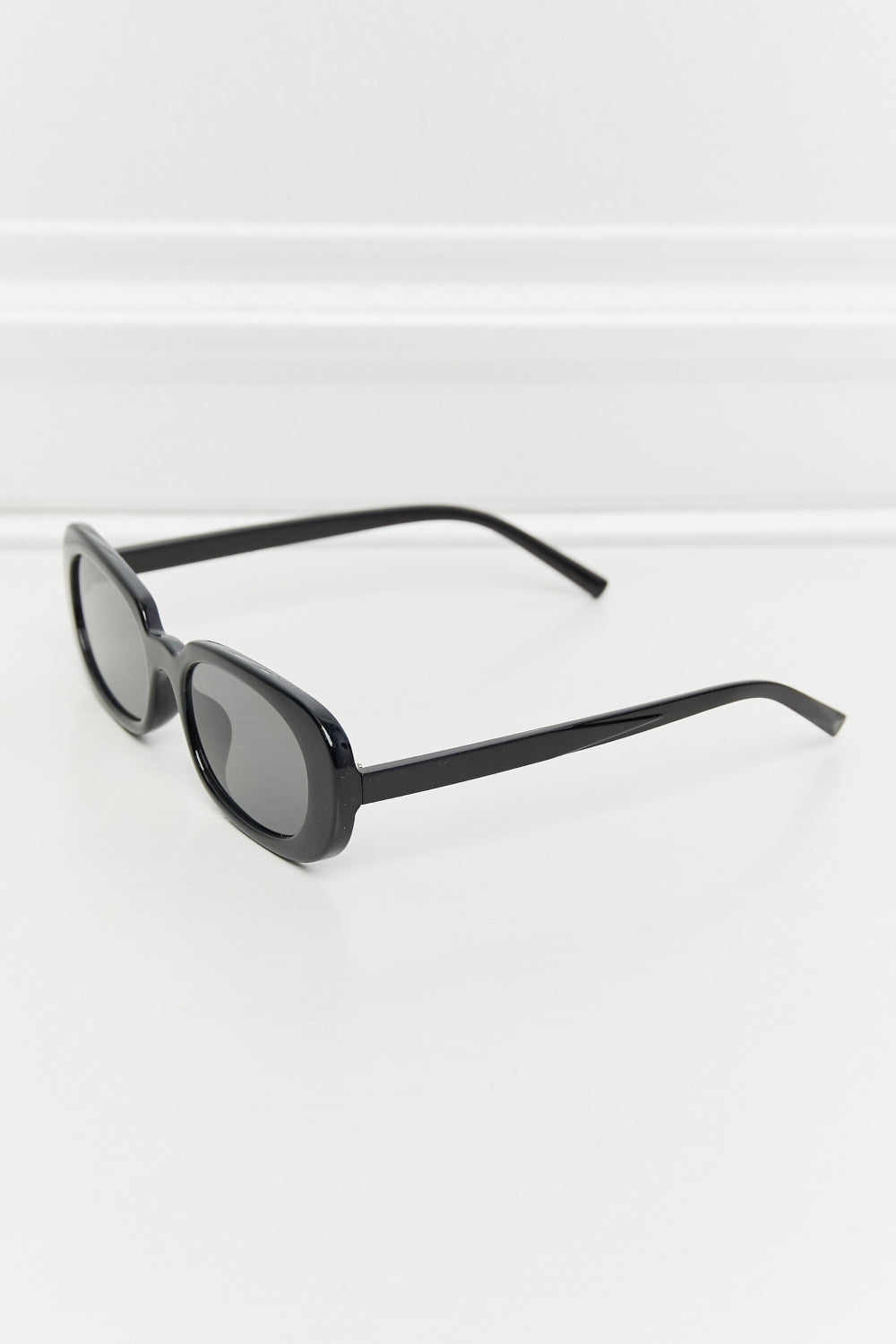 Black oval full-rim sunglasses with softly curved dark lenses, a polished frame, and slender temples displayed at an angled perspective.