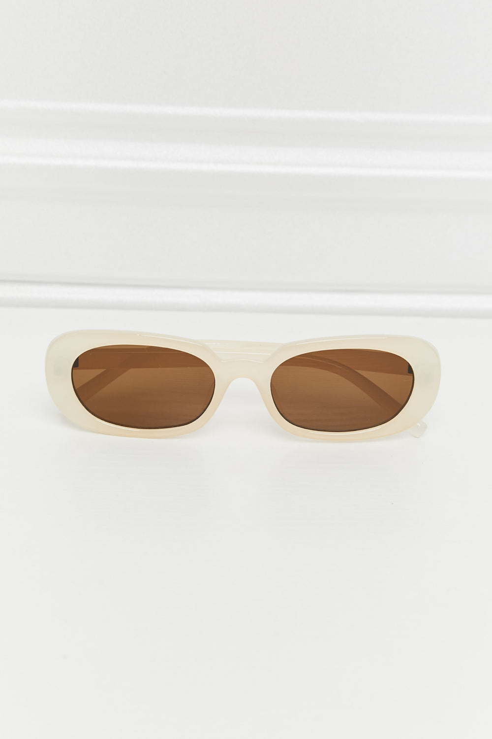 Cream oval full-rim sunglasses feature a softly curved, chunky polycarbonate frame and warm brown lenses in a polished vintage-inspired silhouette.