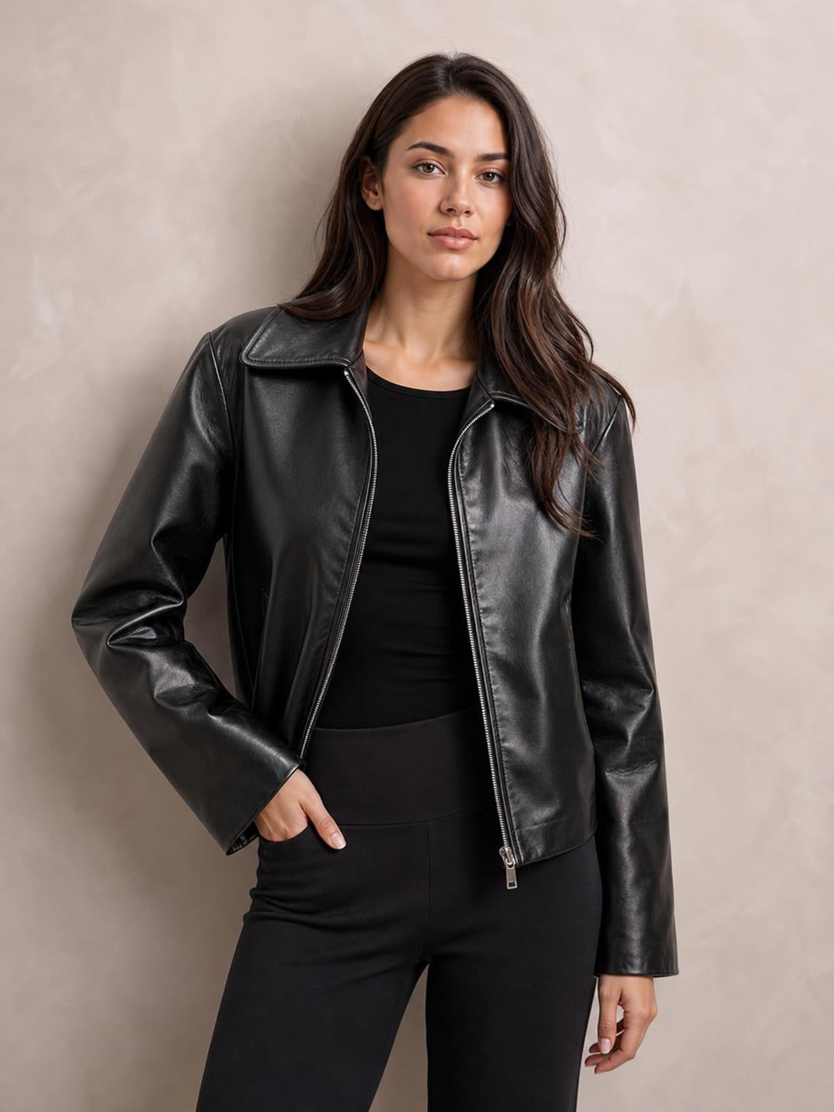 Model poses with one hand in her pocket wearing a black oversized faux leather moto jacket, featuring a wide collar, long sleeves, and open zip front.