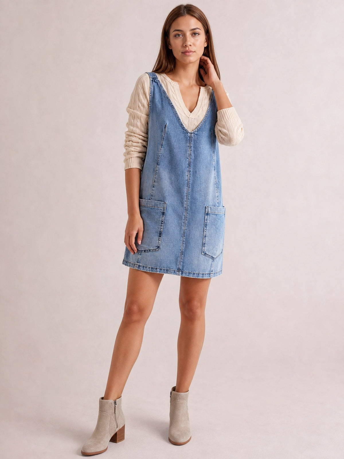 Model wears a light blue oversized V-neck denim tank dress with a relaxed above-knee silhouette, front patch pockets, and visible seam construction.