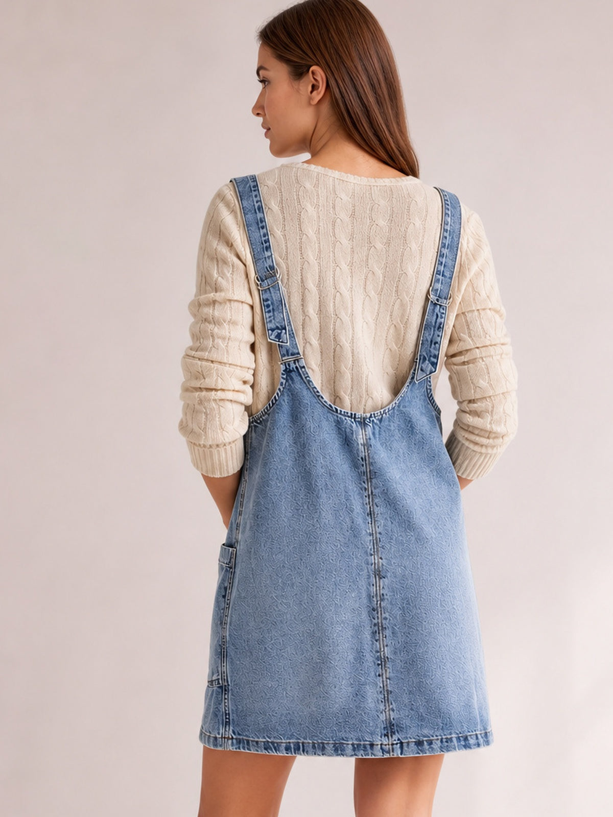 Model shown from behind in a light blue oversized denim tank dress with adjustable shoulder straps, a relaxed above-the-knee A-line silhouette, and visible side pocket.