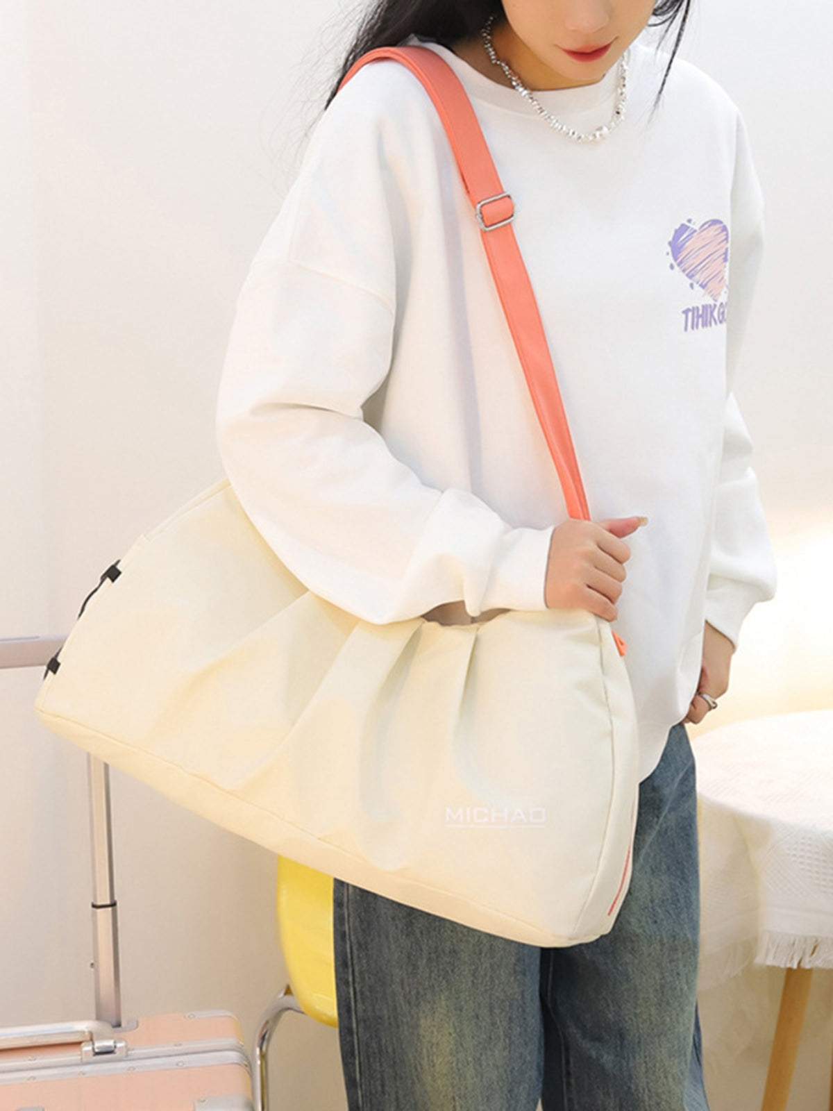 A model holds a large cream Oxford cloth crossbody bag with a relaxed slouched silhouette, roomy construction, and a long coral adjustable strap.