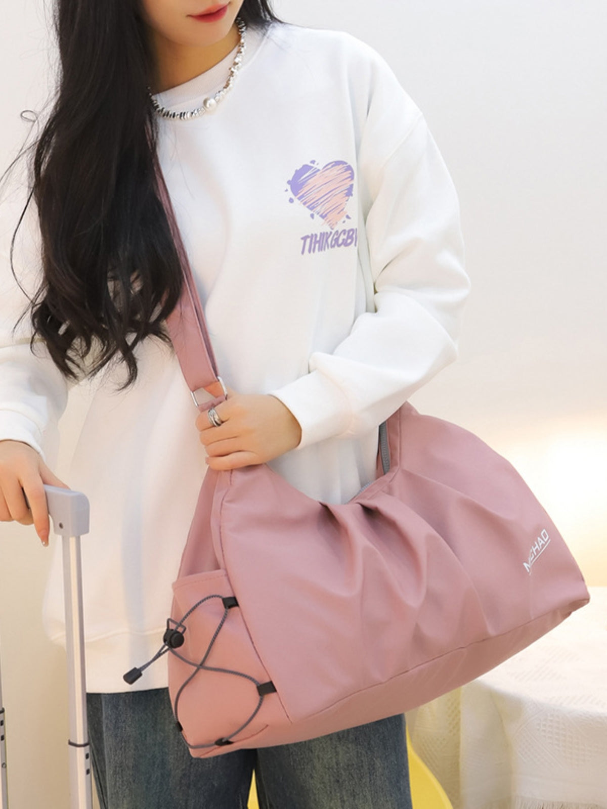 A model carries a large pink Oxford cloth crossbody bag with an adjustable strap, softly slouched silhouette, gathered front, and roomy construction.