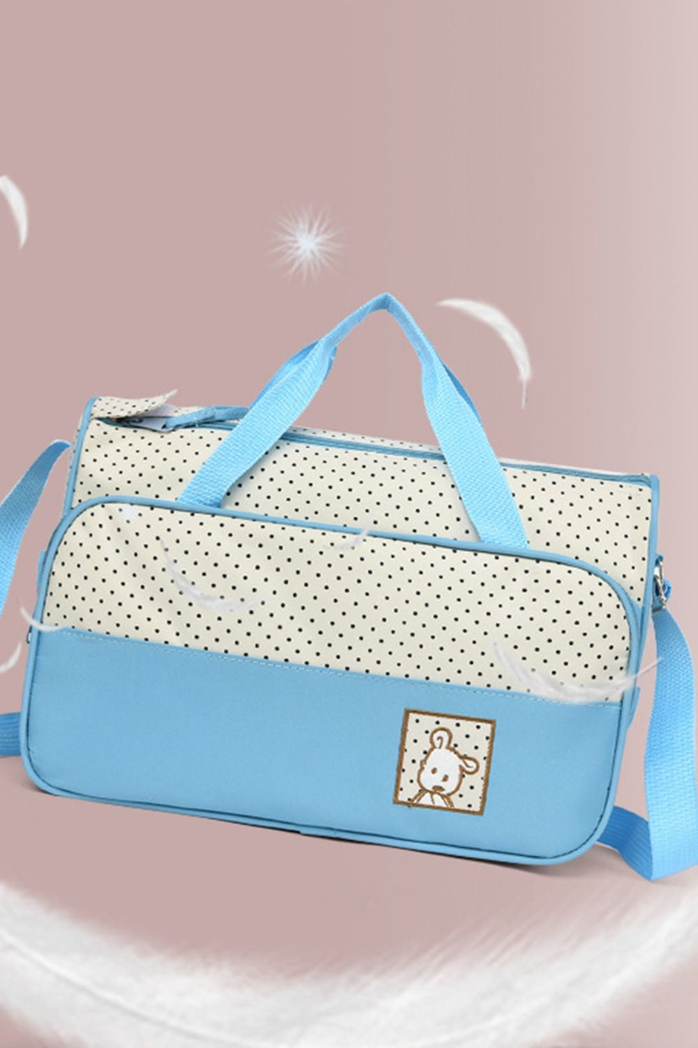 A large blue Oxford cloth tote features a softly structured silhouette, contrasting polka-dot panels, two top handles, and a long shoulder strap.