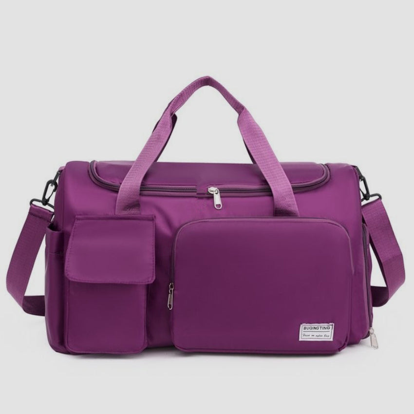 Oversize purple oxford cloth travel bag with a structured silhouette, dual top handles, detachable shoulder strap, wide zippered opening, and multiple front pockets.