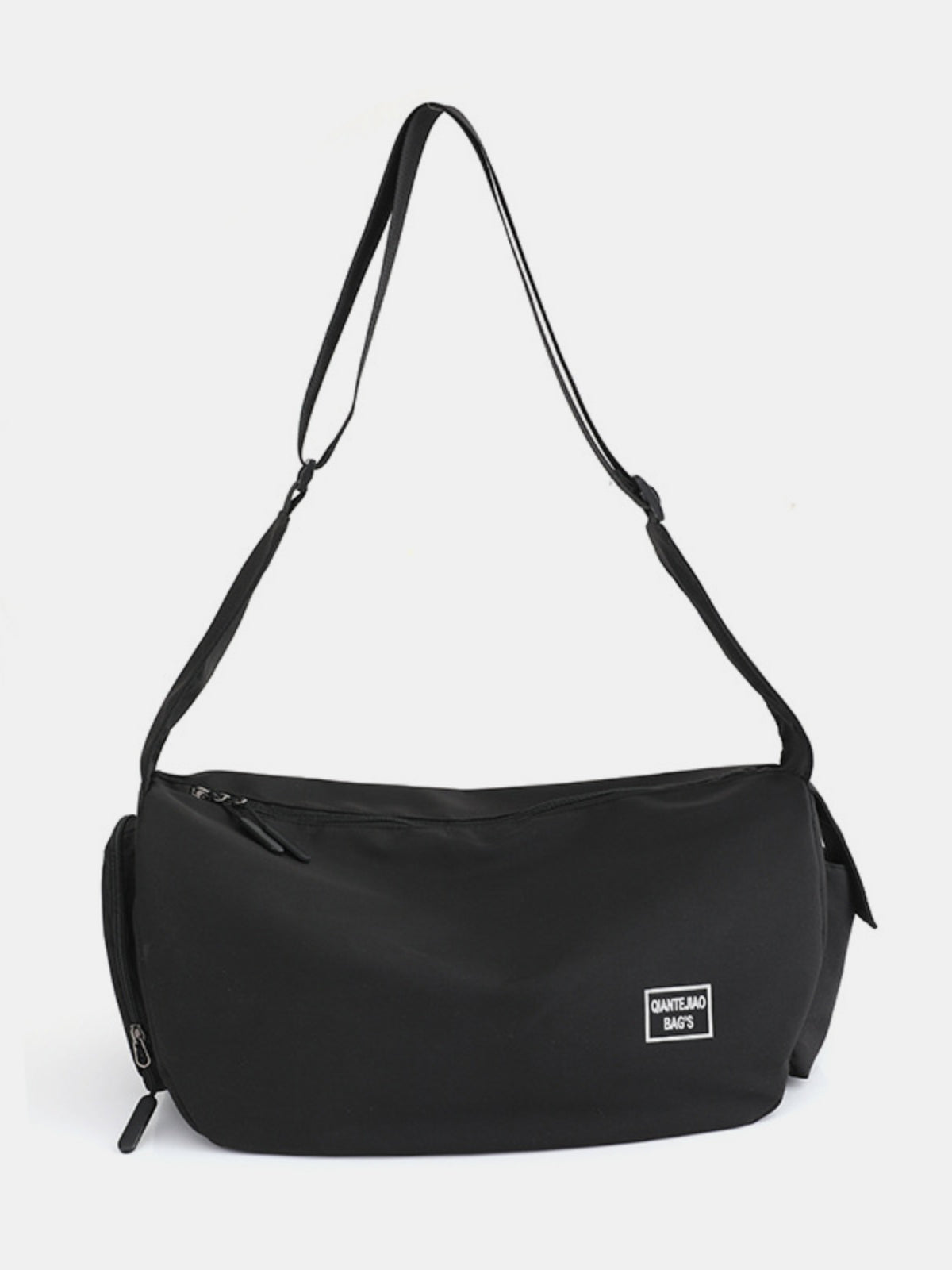 A large black Oxford cloth crossbody bag features a softly curved, gently slouching silhouette, long strap, zip-top opening, and visible external zip compartments.