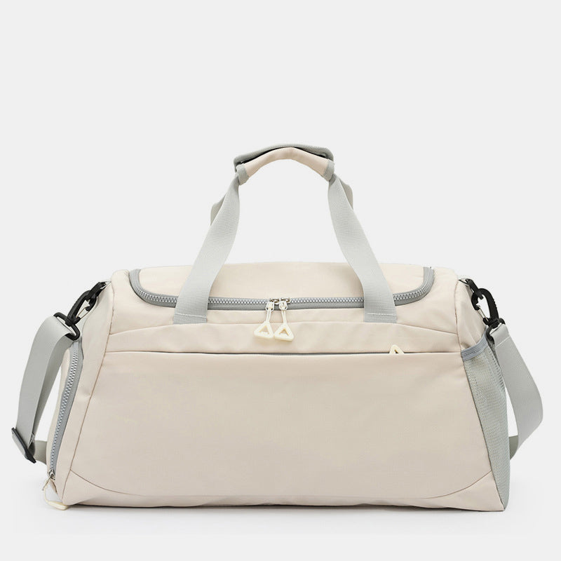 An oversize beige Oxford cloth travel bag features a roomy duffel silhouette, dual top handles, adjustable shoulder strap, and multiple zippered pockets.