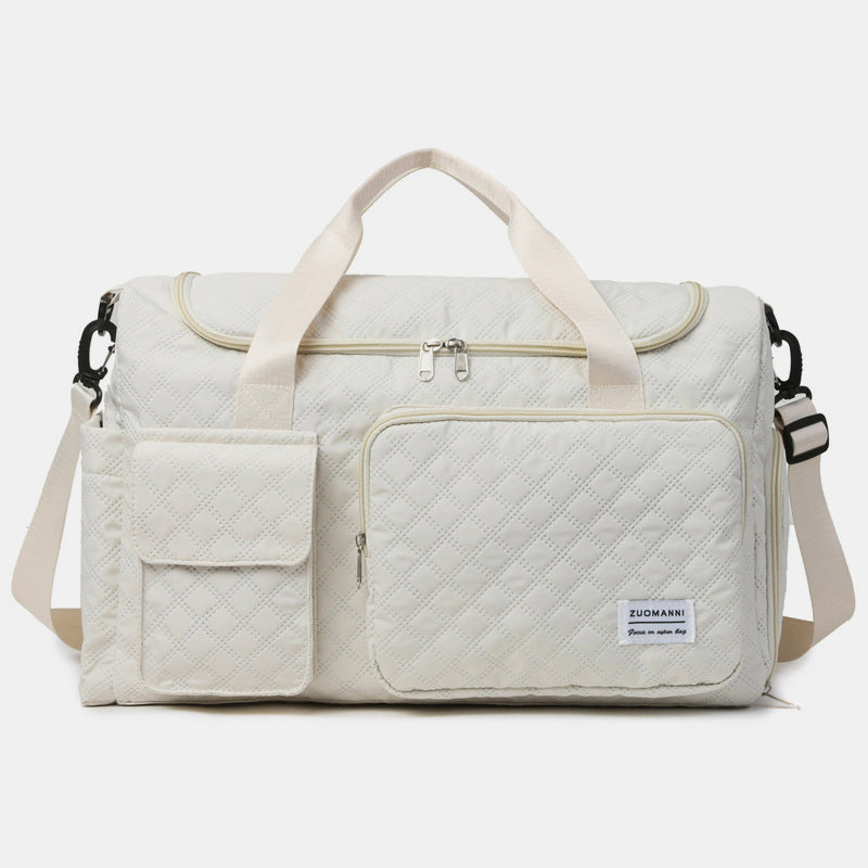 Oversize white quilted Oxford cloth travel bag with dual top handles, an adjustable shoulder strap, zip-top closure, and multiple exterior pockets.