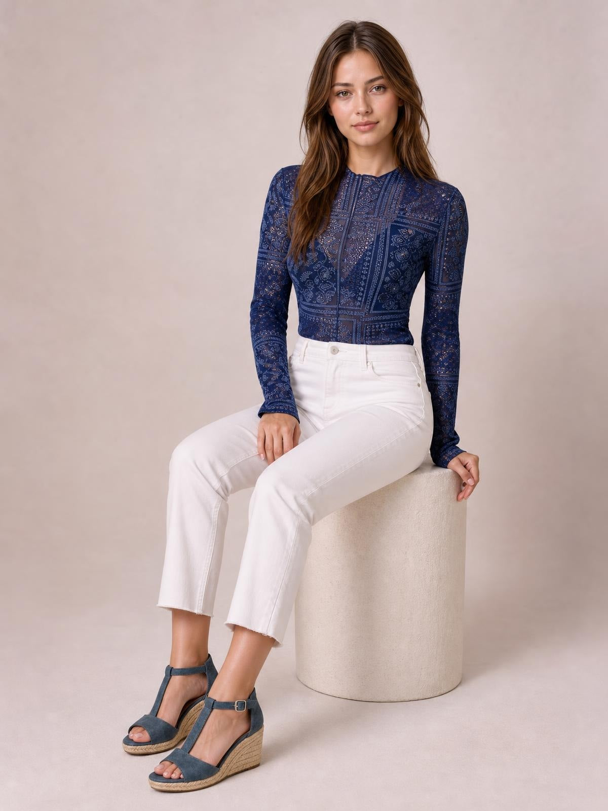 Seated model wears a fitted navy paisley mock neck sheer top with long sleeves, a close silhouette, and delicate printed construction.