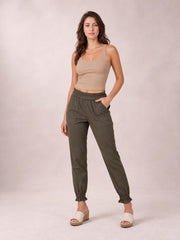 Model poses in olive green paperbag waist pants with side pockets, relaxed straight-leg silhouette, elasticized gathered waistband, and ruched ankle cuffs.