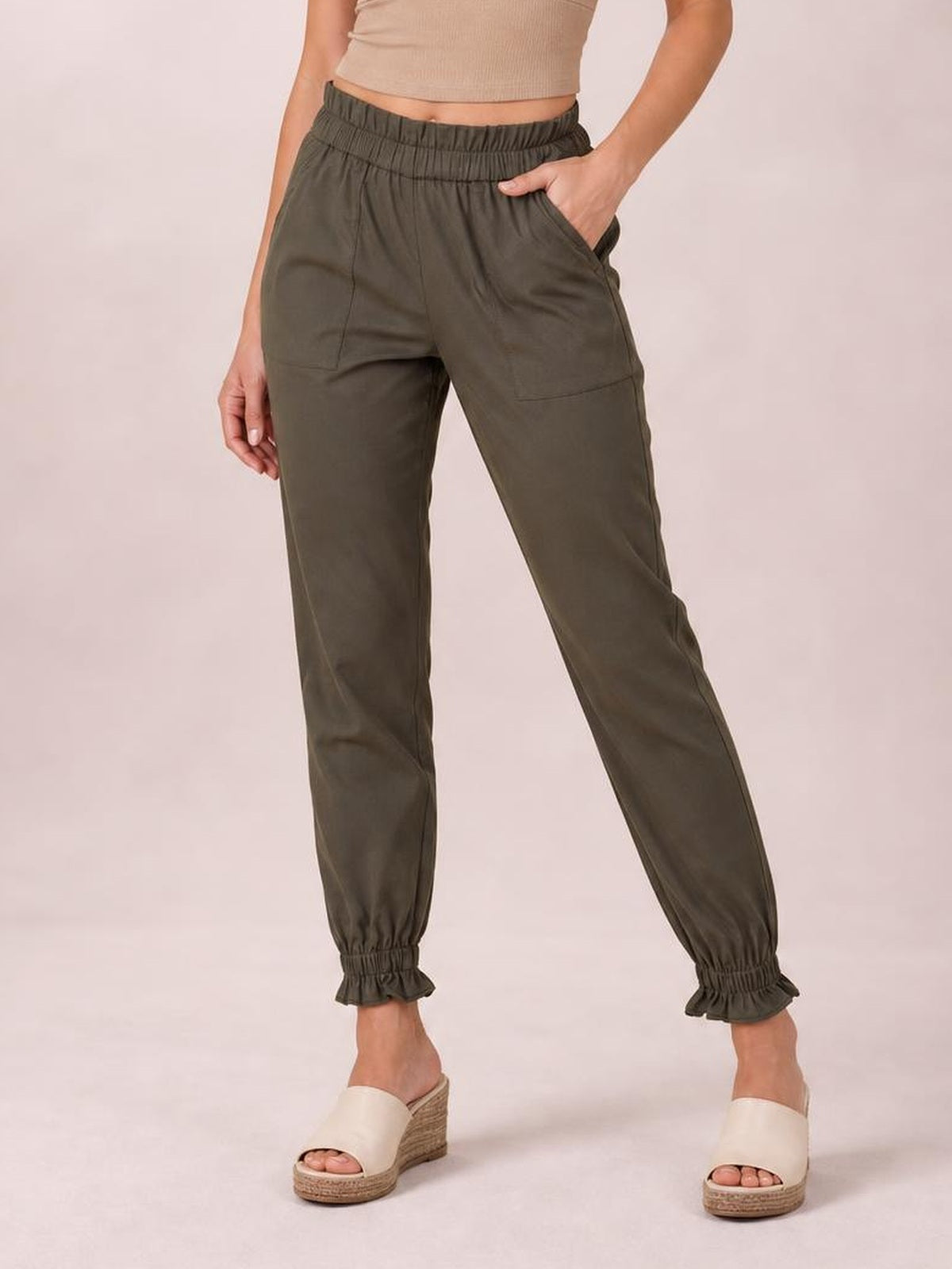 A model poses in olive paperbag waist pants with side pockets, a gathered high waist, relaxed straight-leg silhouette, and elasticized ankle cuffs.