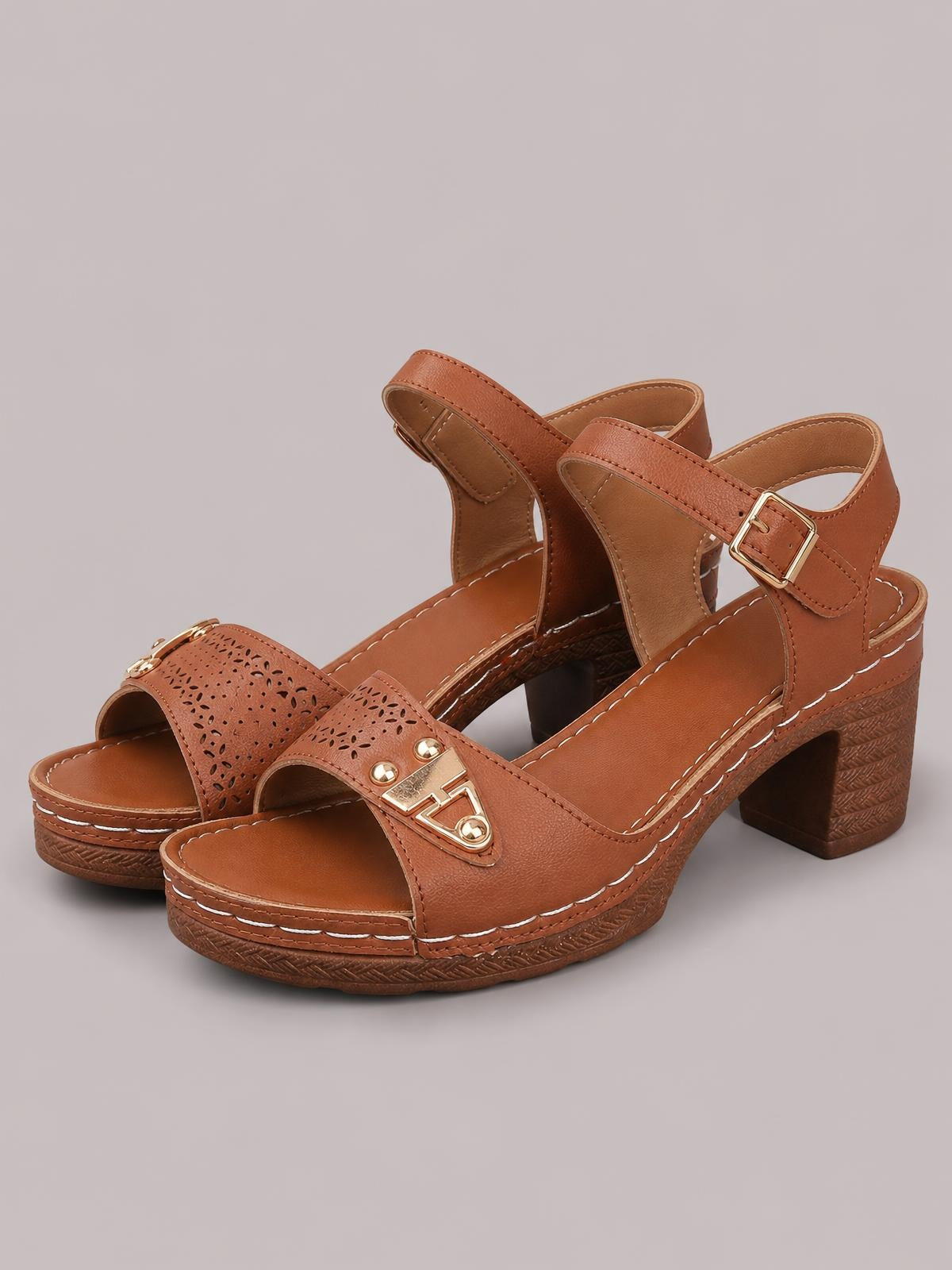 Brown peep-toe block heel sandals feature perforated front straps, adjustable ankle buckles, stitched construction, and mid-height textured heels.