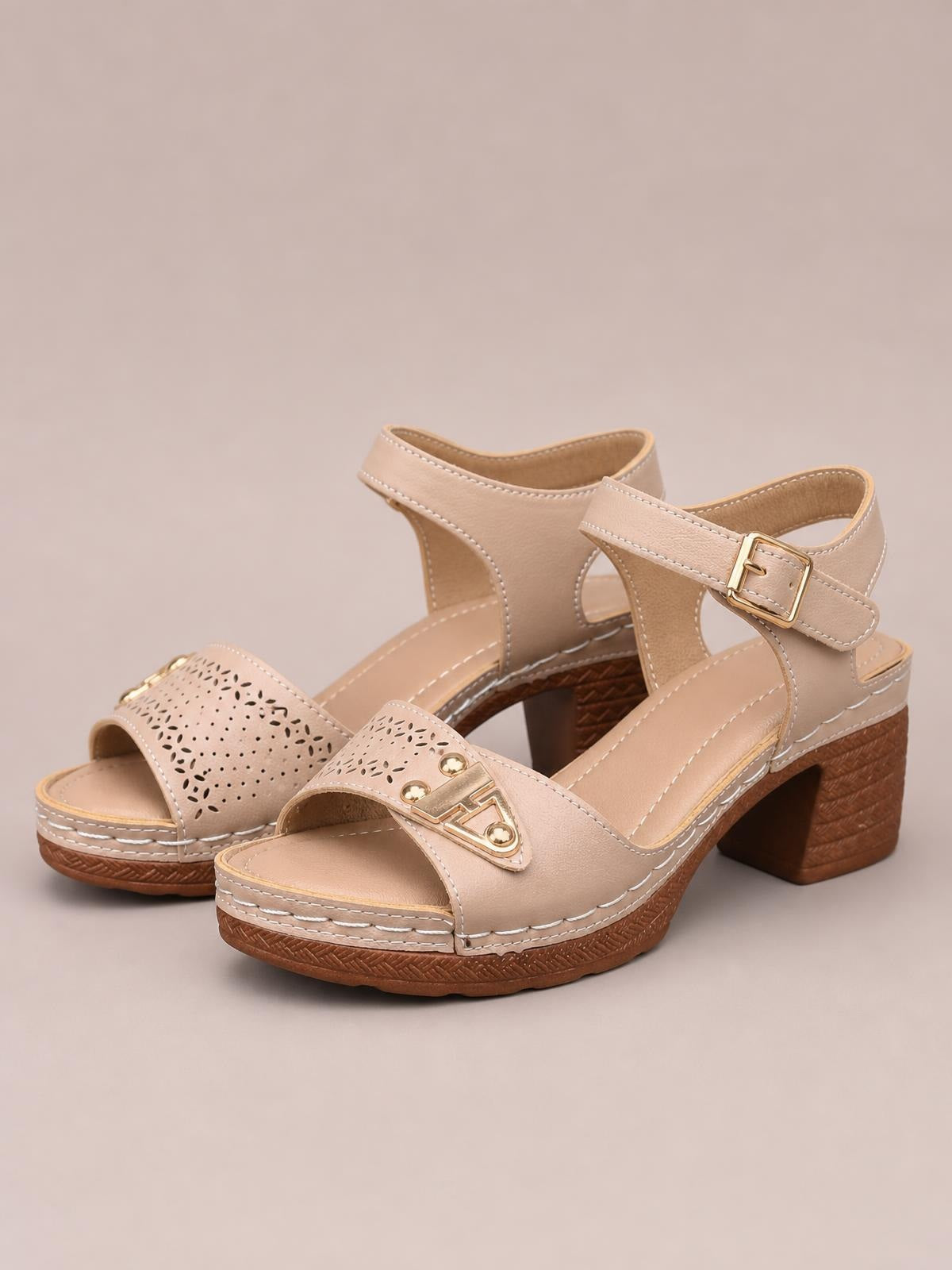 Beige peep toe block heel sandals with ankle buckle straps, decorative gold-tone accents, perforated detailing, stitched midsoles, and sturdy wood-look heels.